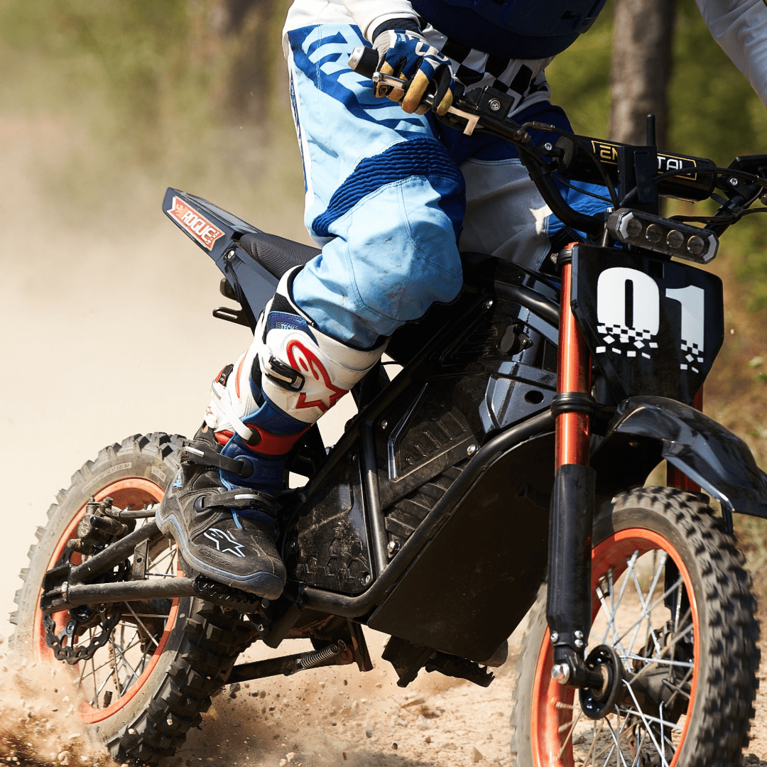 Close-up of Rogue MX-01 electric dirt bike with rider leaning on dirt trail, showcasing suspension and tires