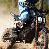 Close-up of Rogue MX-01 electric dirt bike with rider leaning on dirt trail, showcasing suspension and tires