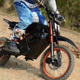 Rider accelerating Rogue MX-01 electric dirt bike on rough rocky path, showcasing 3000W motor power
