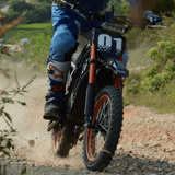 Rogue MX-01 electric dirt bike climbing rocky uphill trail, LED headlight on, perfect for off-road riding
