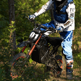 Rogue MX-01 electric dirt bike with 3000W mid-drive motor ridden through forest trail, off-road adventure
